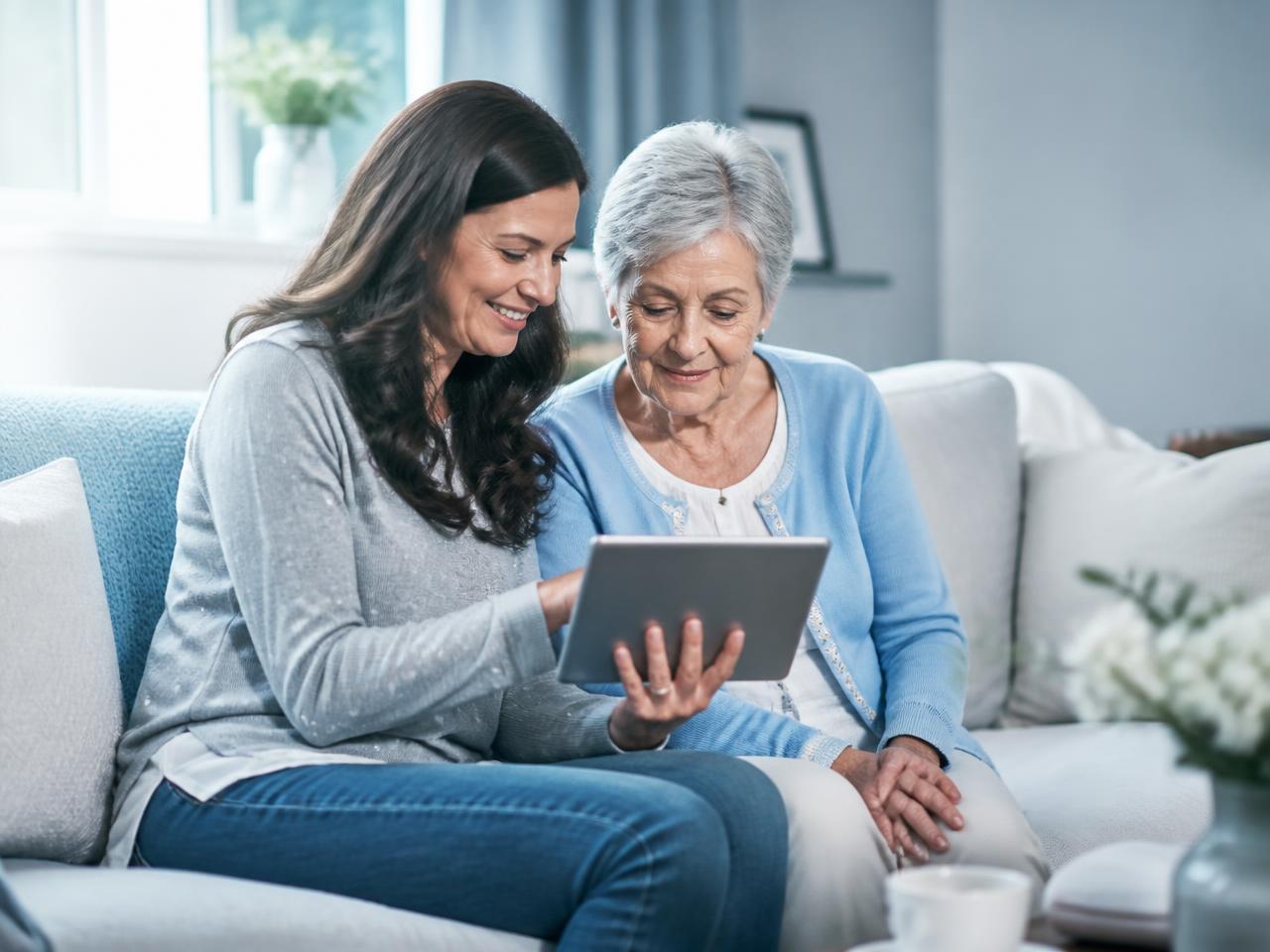 An adult daughter and her elderly mother reviewing health information together on a tablet